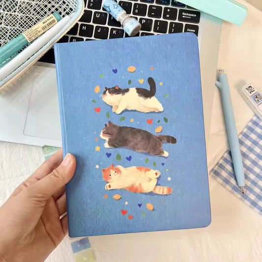 Blue notebook with cute cat illustrations, held over laptop, Soulpurrpose pet lover gift